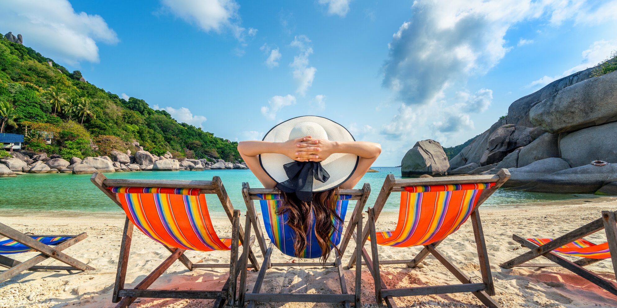 Woman with hat sitting on chairs beach in beautiful tropical bea